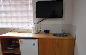 Una cuina americana compacta amb frigorífic integrat, un rentapeus i un televisor penjat a la paret.