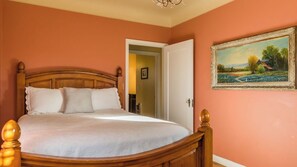 A bedroom with a wooden bed, a door leading to another room, and a framed landscape painting on the wall. - The Cottage at Capitol Hill by Avantstay Group Retreat + Yard Walk to Paso (Paso Robles)