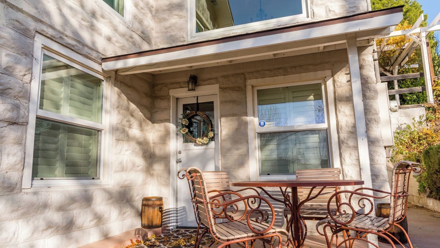 A stone building with a covered patio, a table with chairs, and a wreath on the door.