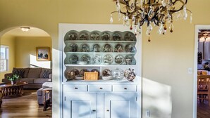 A dining area with a white cabinet displaying china, a chandelier, and a sofa in the background. - The Cottage at Capitol Hill by Avantstay Group Retreat + Yard Walk to Paso (Paso Robles)