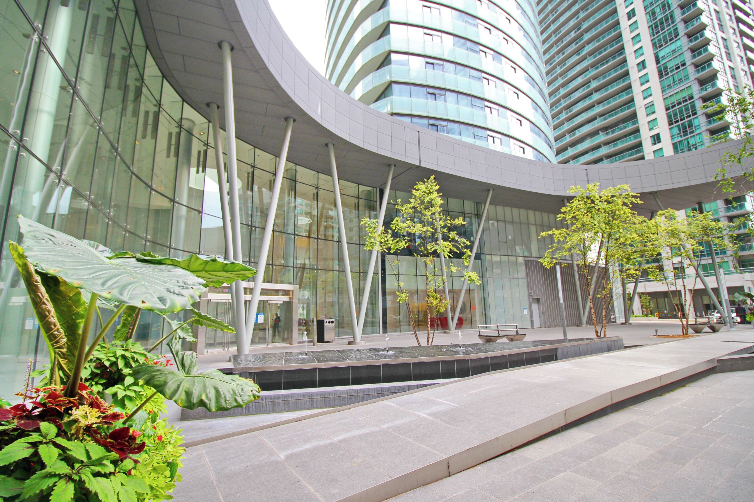 Un edificio moderno con fachada curva, amplios ventanales de vidrio y una fuente central con árboles.