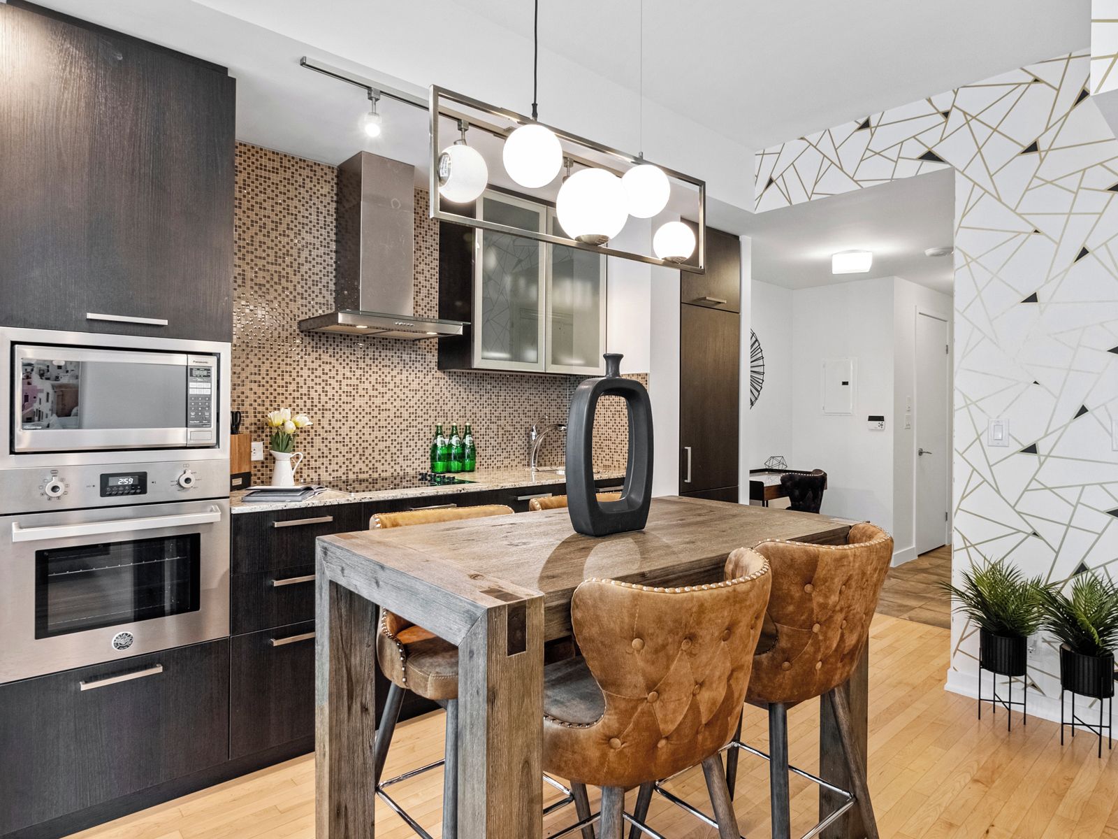 A modern kitchen with a built-in microwave, oven, and a wooden dining table with two chairs.