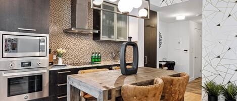 A modern kitchen with a built-in microwave, oven, and a wooden dining table with two chairs.