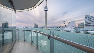 A balcony with a glass railing overlooking a cityscape, including a tower and construction sites.