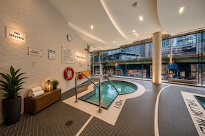 Una piscina interior con un flotador salvavidas, un reloj y señales de seguridad en las paredes.