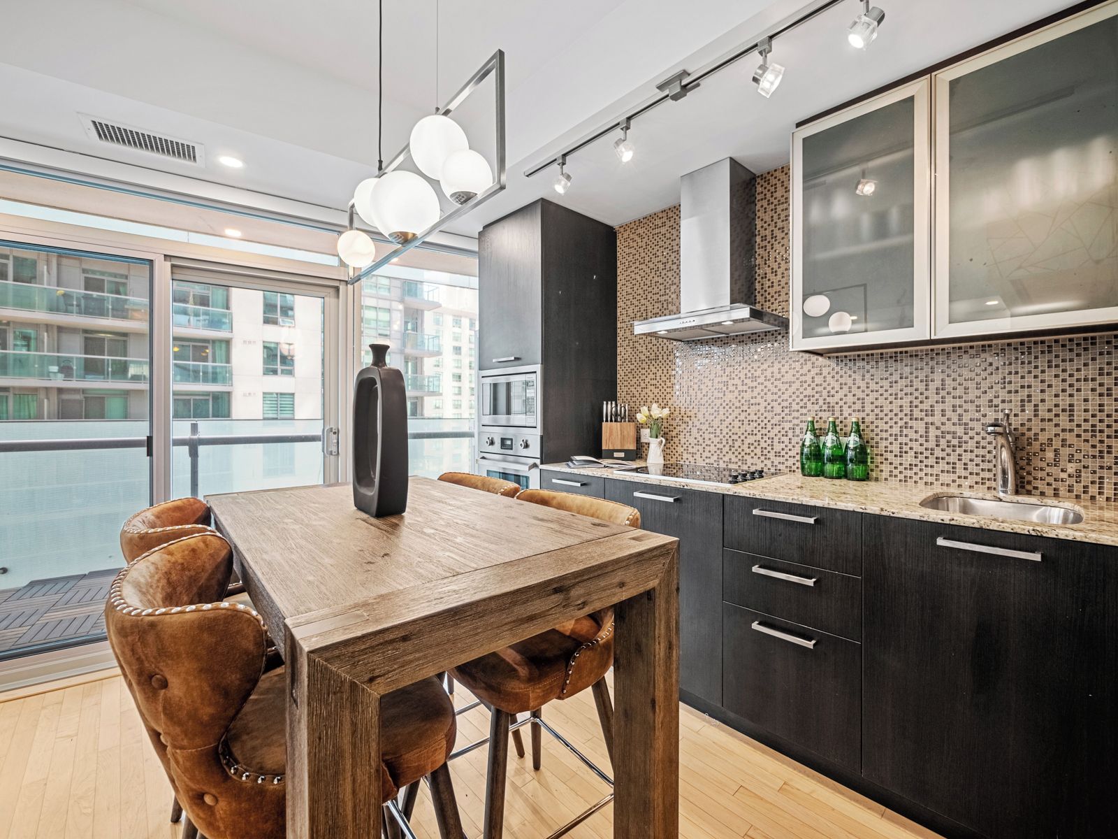 Cozinha moderna com mesa de jantar de madeira, armários escuros e uma grande janela com vista para a paisagem urbana.