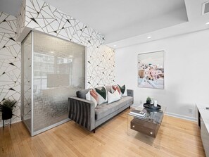 Una sala de estar moderna con un sofá gris, una mesa de centro de vidrio y un diseño geométrico en la pared.