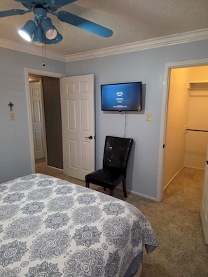 A bedroom with a bed, a television mounted on the wall, a ceiling fan, and a door leading to another room. - Charming 3 bedroom house in peaceful Lubbock neighborhood (Lubbock)