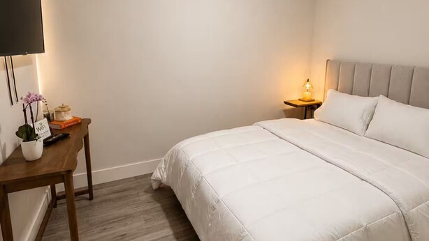 Une chambre à coucher comprenant un lit, une table de chevet, un bureau, un ventilateur de plafond et un téléviseur fixé au mur.