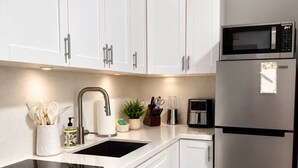 Une cuisine avec des armoires blanches, un réfrigérateur en acier inoxydable, un four à micro-ondes, un évier et un plan de travail sur lequel se trouvent divers objets.