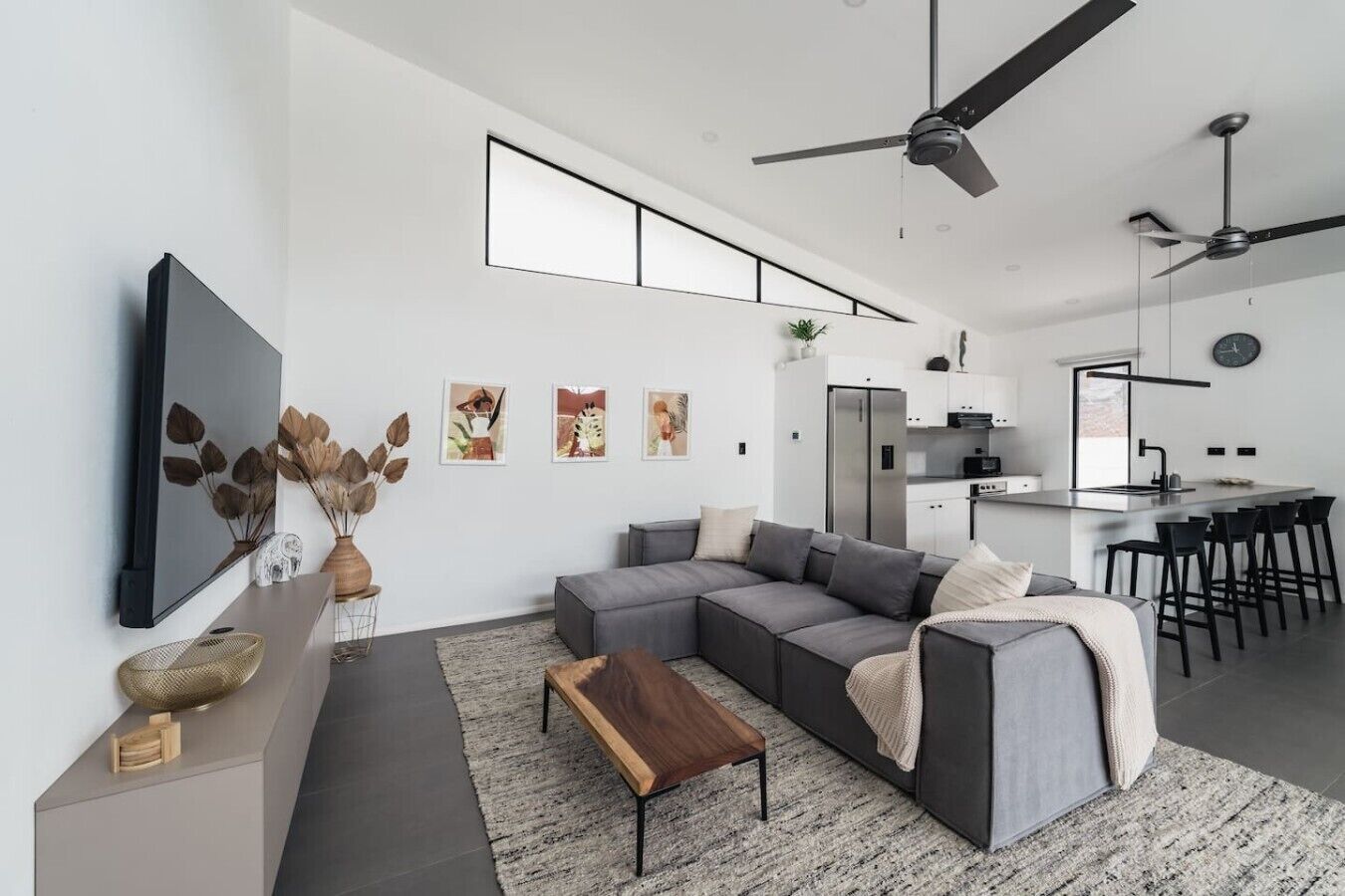 A modern living room with a sectional sofa, a coffee table, and a kitchen area with a refrigerator and bar stools.