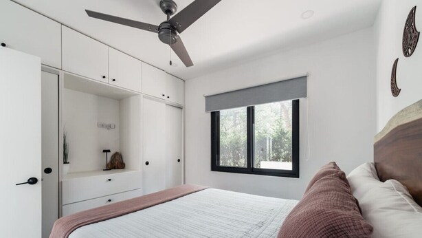 Ein Schlafzimmer mit Bett, Deckenventilator, Fenster und Einbauschränken.