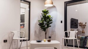 Ein modernes Interieur mit einem weißen Tisch, zwei weißen Stühlen, einer Topfpflanze und einer Pendelleuchte.