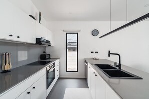 A modern kitchen with white cabinetry, a black countertop, a built-in oven, a toaster, and a window with a view. - Modern Villa | Private Pool | Near Playa Grande (Matapalo)