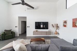 Ett modernt vardagsrum med en grå soffa, en grön fåtölj, ett träbord och en platt-TV som är monterad på väggen.