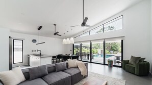 Ein zeitgemäßer Wohnbereich mit grauem Sofa, Essbereich und Blick auf einen Swimmingpool.