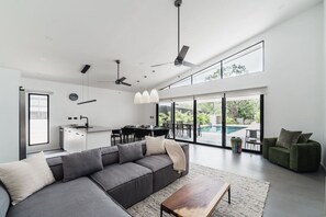 Ein zeitgemäßer Wohnbereich mit grauem Sofa, Essbereich und Blick auf einen Swimmingpool.