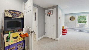 Un pasillo con una puerta que da a una habitación, un aro de baloncesto y una máquina recreativa Big Buck's.