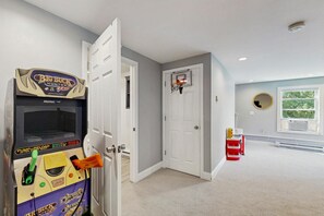 Ein Flur mit einer Tür zu einem Zimmer, einem Basketballkorb und einer Big Buck’s Arcade-Maschine.