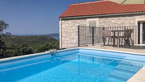 A swimming pool with a clear view of the landscape, a stone building with a red-tiled roof, and outdoor furniture. - Lovely home in Zaostrog with house sea view (Zaostrog)