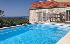 Ein Swimmingpool mit freiem Blick auf die Landschaft, ein Steinhaus mit rotem Ziegeldach und Gartenmöbel.