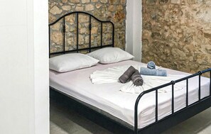 Ein Bett mit Steinwand im Hintergrund, einem Metall-Kopfstück und weißen Bettwäsche.
