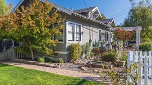 A two-story house with a front porch, a small garden with a variety of plants, and a white picket fence. - Poe House by Avantstay 1916 Craftsman Downtown Paso (Paso Robles)
