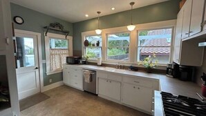 A kitchen with white cabinets, a stove, and a window with curtains. - Poe House by Avantstay 1916 Craftsman Downtown Paso (Paso Robles)