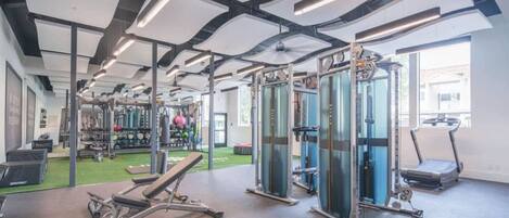 Une salle de sport équipée de matériel d’exercice, d’un tapis de course et d’un espace recouvert d’une moquette artificielle verte.