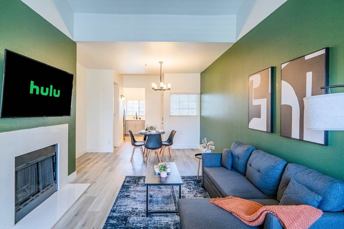 A modern living room with a flat-screen TV, a fireplace, a sofa, and a dining area with chairs and a table.