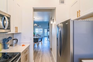 Uma cozinha moderna com eletrodomésticos de aço inoxidável, um espaço de refeições com mesa e cadeiras, e vista para a sala de estar.