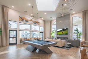 Uma sala de estar moderna com mesa de bilhar, assentos confortáveis, janelas amplas e uma televisão.