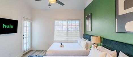 A hotel room with two beds, a ceiling fan, a large window, and a wall-mounted TV displaying 'hulu'.