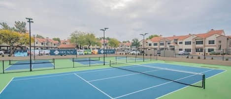 An outdoor tennis court with multiple courts, surrounded by residential buildings.