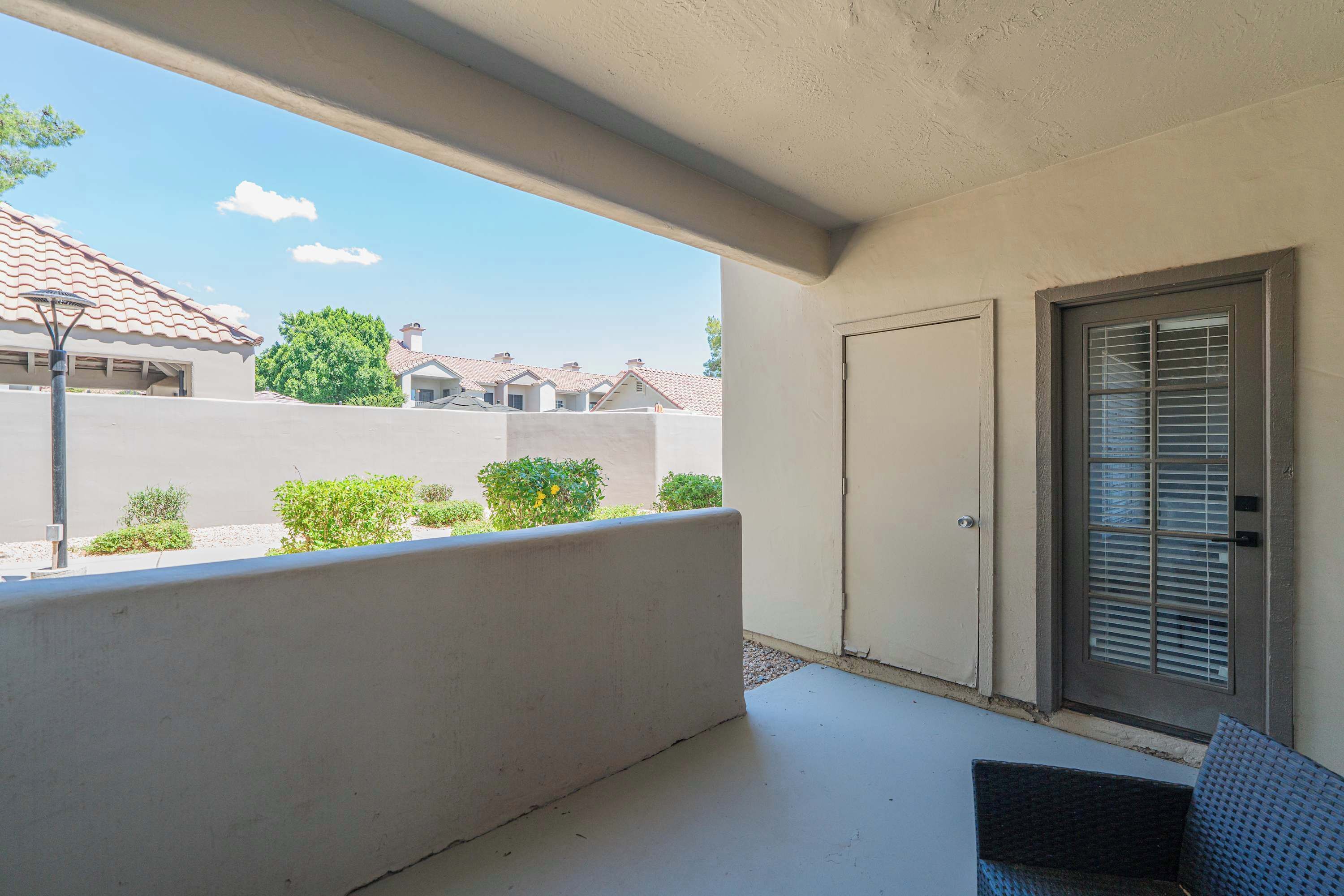 A balcony with a view of neighboring houses, a door with a window, and a small outdoor area with plants.