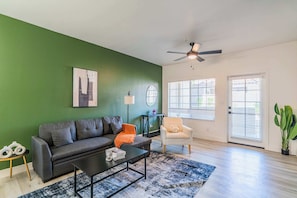 Uma sala de estar com parede verde, sofá cinza, mesa de centro e ventilador de teto.