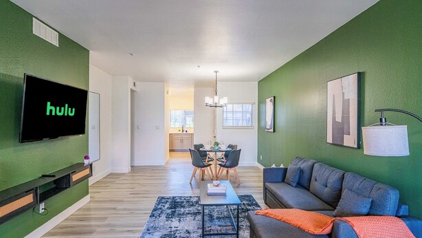 A modern living room with a flat-screen TV, a sofa, a coffee table, and a dining area with chairs and a table. - Princess Dr Retreat Pool Balcony Parking WD WiFi (Scottsdale)