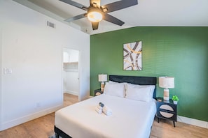 A hotel room with a bed, a ceiling fan, a green accent wall, a painting, and a nightstand with a lamp. - Desert Oasis Near TPC Poo Balcony Parking WD (Scottsdale)