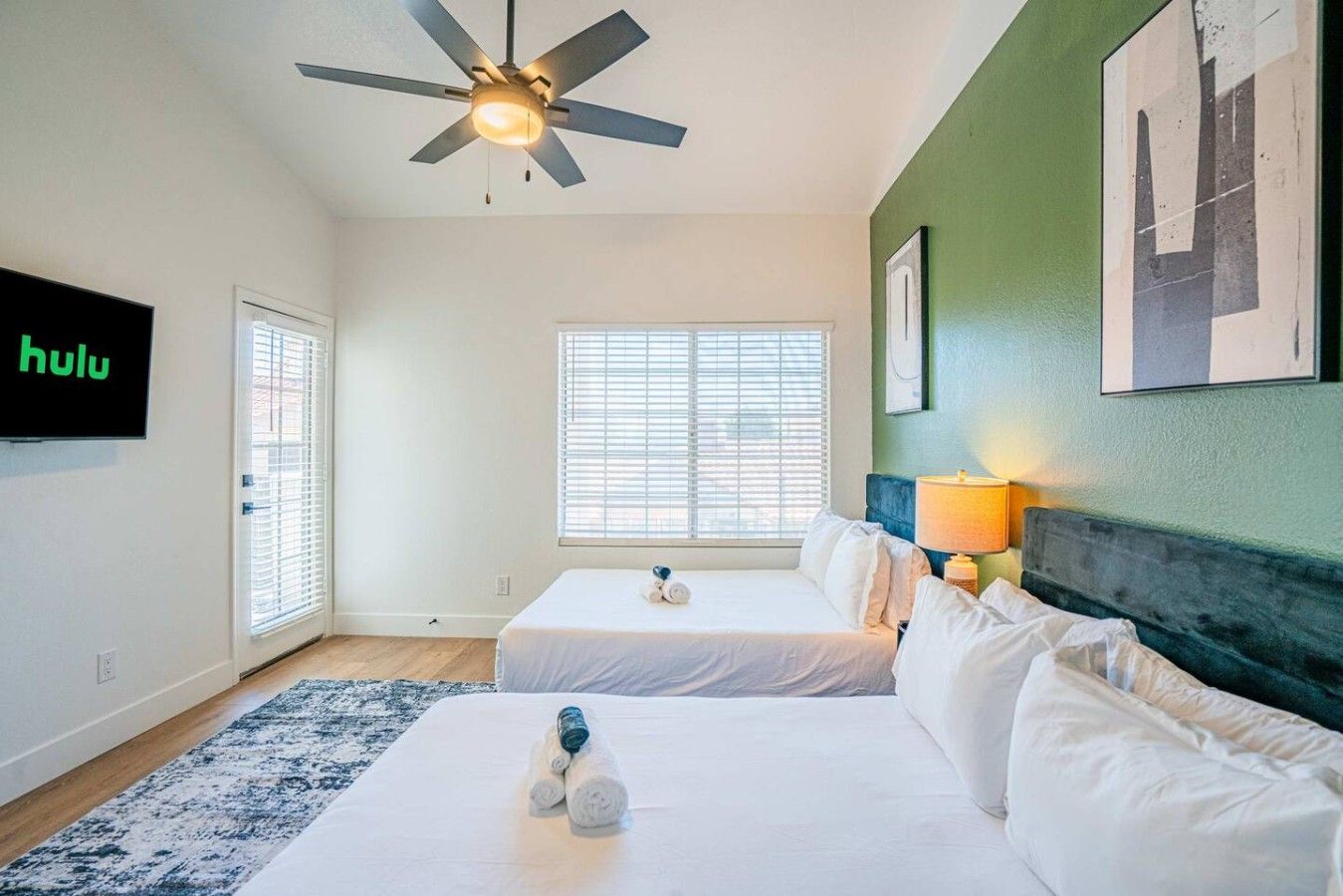A hotel room with two beds, a ceiling fan, a TV, and a window with blinds.