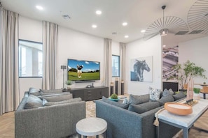 Una sala de estar moderna con un televisor de pantalla plana grande, sofás grises, una mesa de centro y una zona de comedor con una planta y velas.