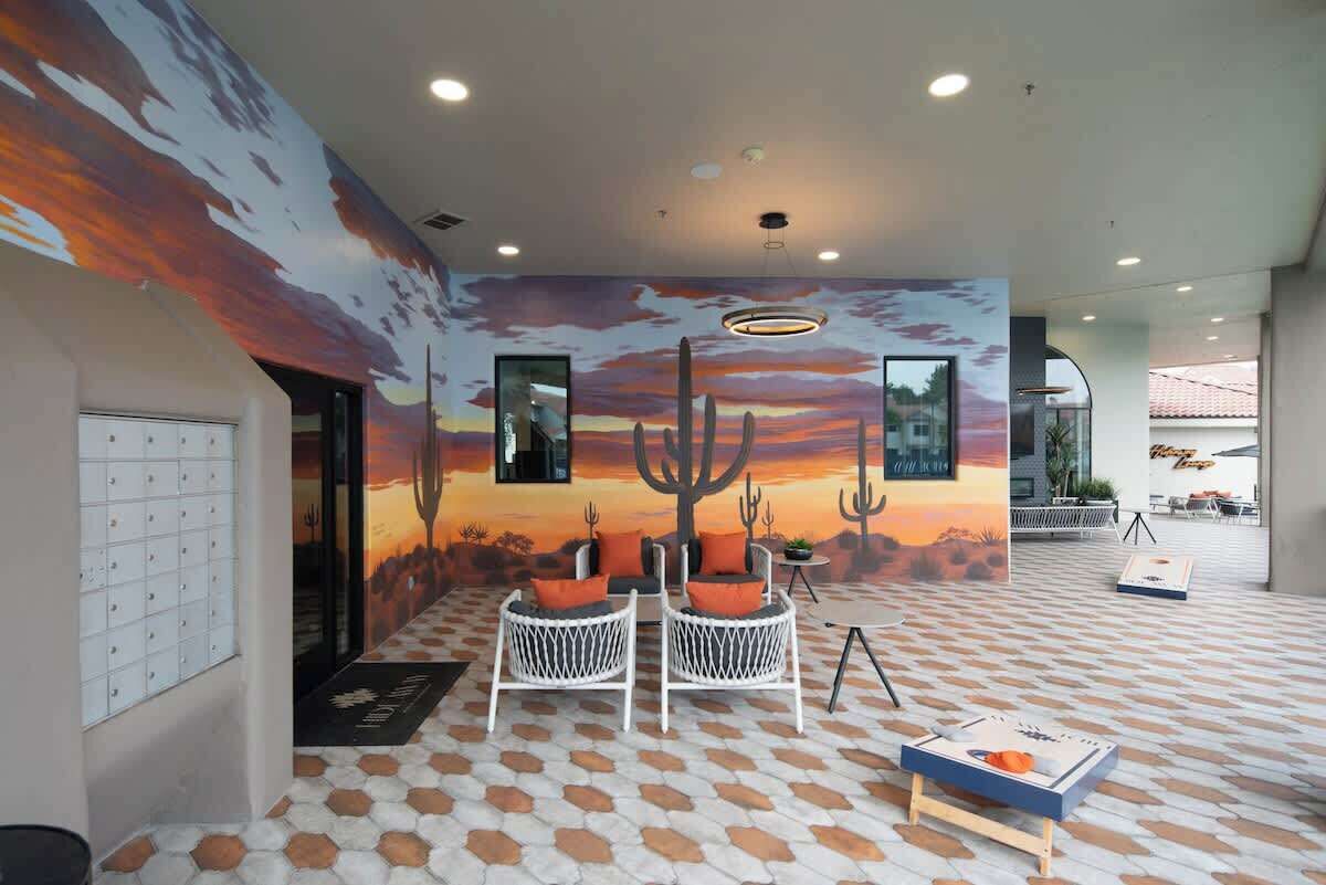 Un hall d’entrée orné d’une fresque représentant un coucher de soleil dans le désert, deux fauteuils en osier blanc avec des coussins orange et un sol à motifs.