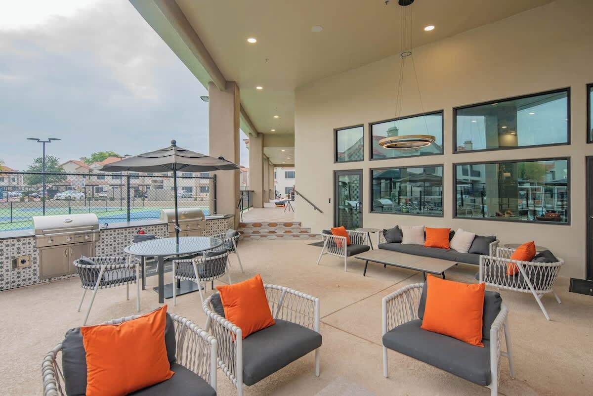 Un patio al aire libre con mobiliario de mimbre, una parrilla y una piscina al fondo.