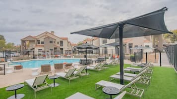Un espace aménagé au bord de la piscine, avec des chaises longues, une piscine et un bâtiment en arrière-plan.