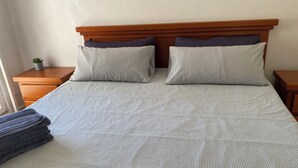 A double bed with a striped bedspread, two pillows, and a small bedside table with a plant. - Monthly Beach House Rental in Manzanillo, Mexico – Perfect for Snowbirds (Manzanillo)