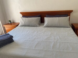 A double bed with a striped bedspread, two pillows, and a small bedside table with a plant. - Monthly Beach House Rental in Manzanillo, Mexico – Perfect for Snowbirds (Manzanillo)