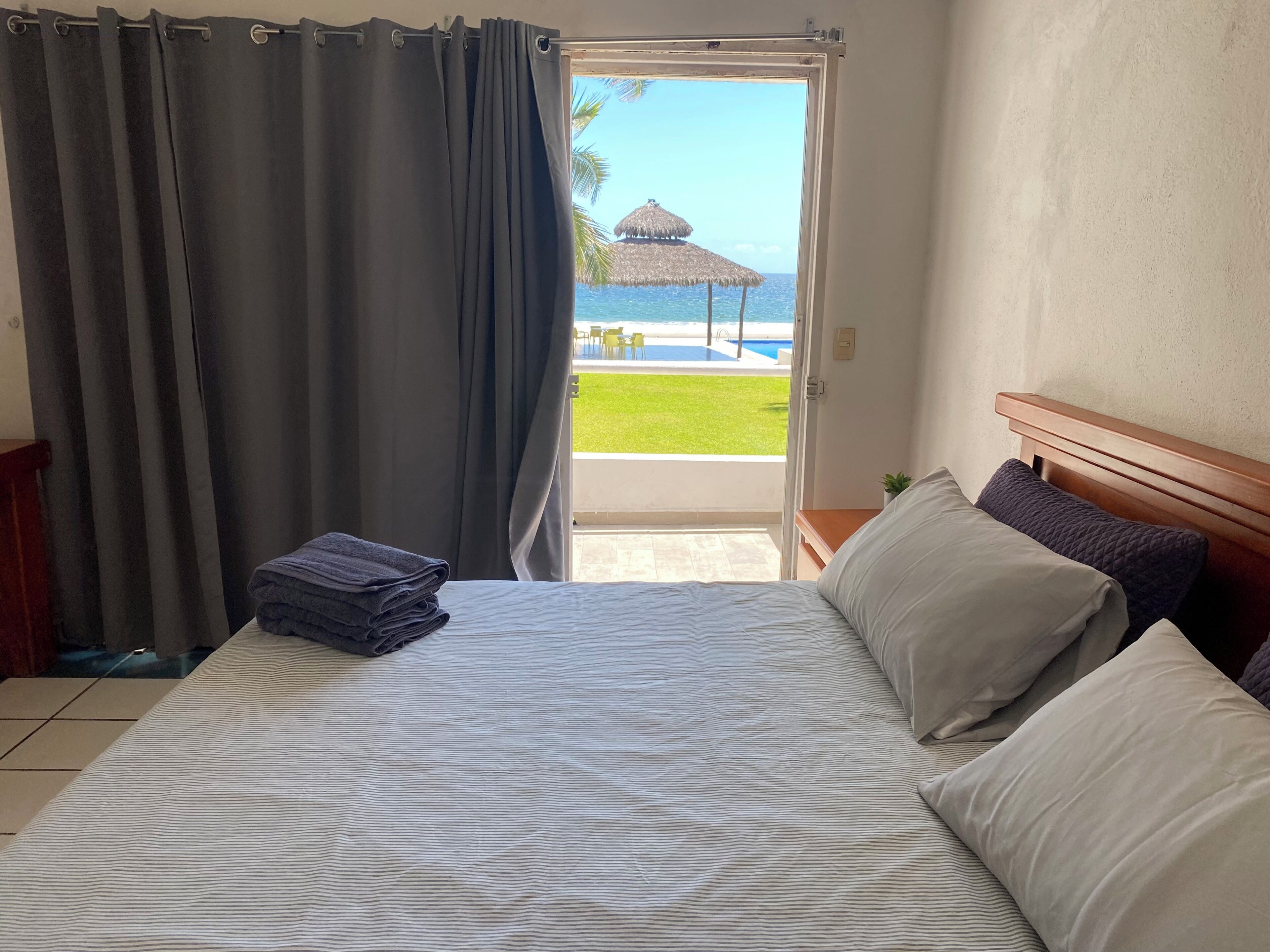 A hotel room with a bed, a neatly folded towel, and a view of a pool and beach.