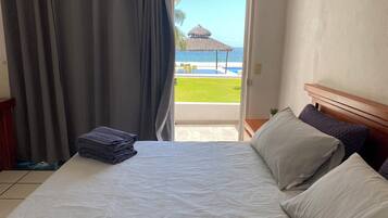 A hotel room with a bed, a neatly folded towel, and a view of a pool and beach.