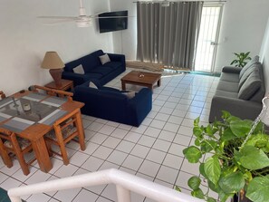 A living room with a blue sofa, a wooden coffee table, a grey sofa, and a TV mounted on the wall. - Monthly Beach House Rental in Manzanillo, Mexico – Perfect for Snowbirds (Manzanillo)