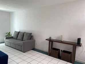 Un salon avec un canapé gris, une petite table et deux paniers en osier.