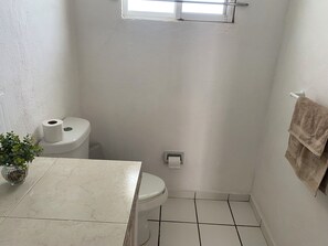 A small, white bathroom with a toilet, a towel rack, and a window.